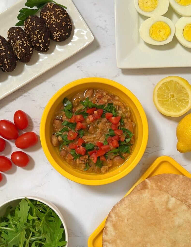 Egyptian ful (fava beans), tameya, eggs, arugula salad, tomatoes, lemon