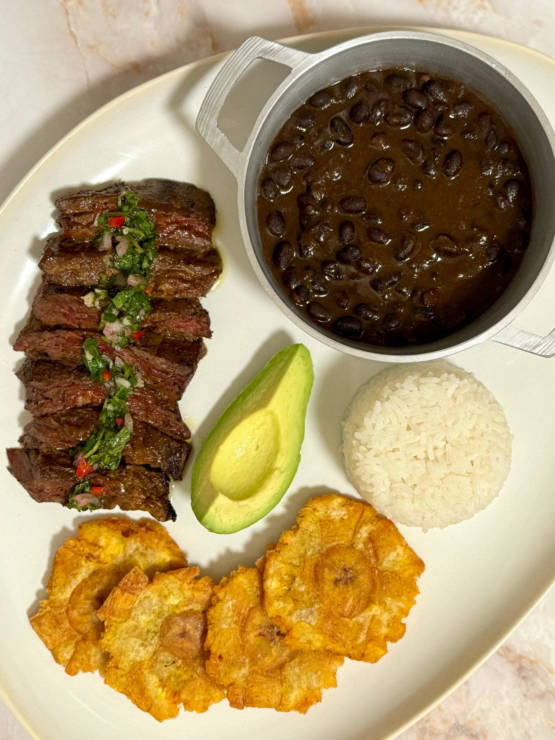 Churrasco with chimichurri sauce, white rice, black beans, tostones, and avocado